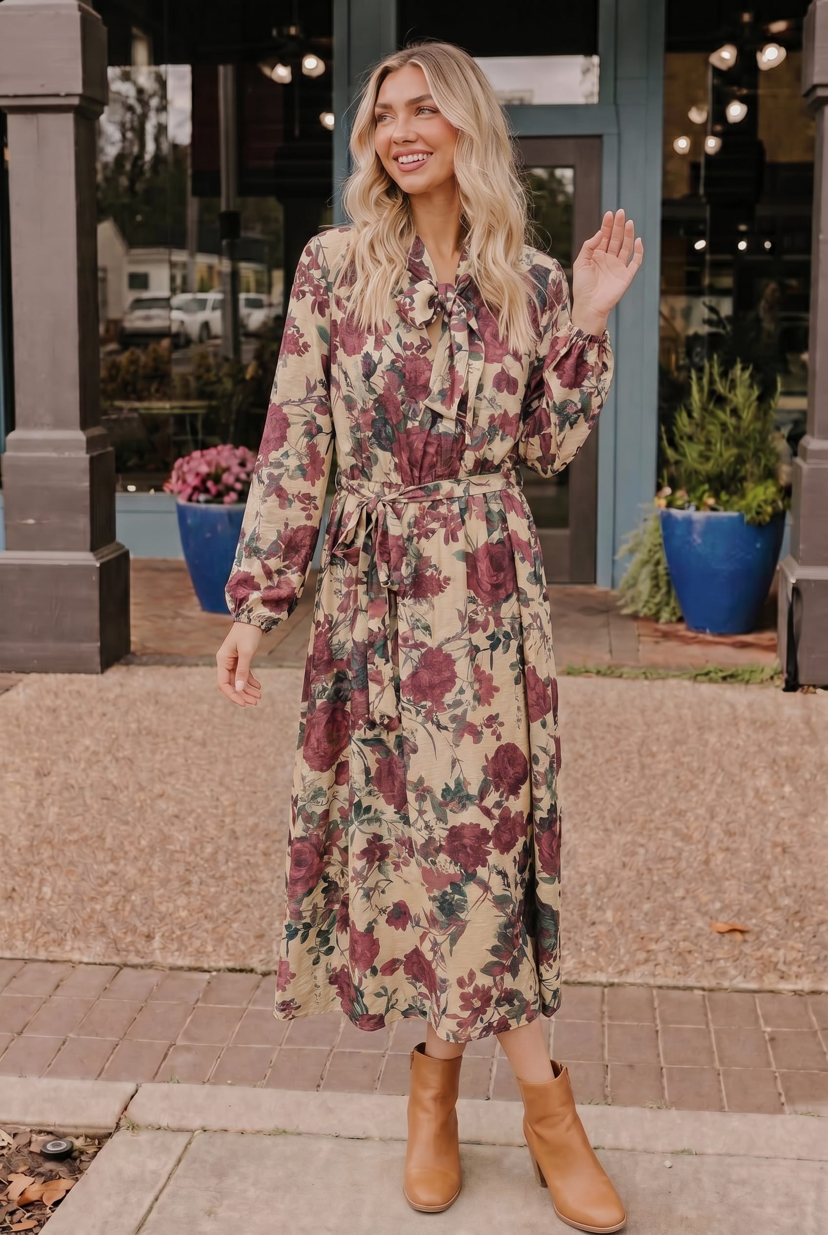Woman in a floral dress standing outdoors on a sidewalk.