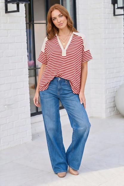 Woman wearing a red and white striped top and blue jeans standing against a white brick wall.