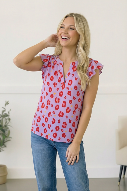 Woman wearing a pink blouse with red floral pattern and blue jeans indoors.