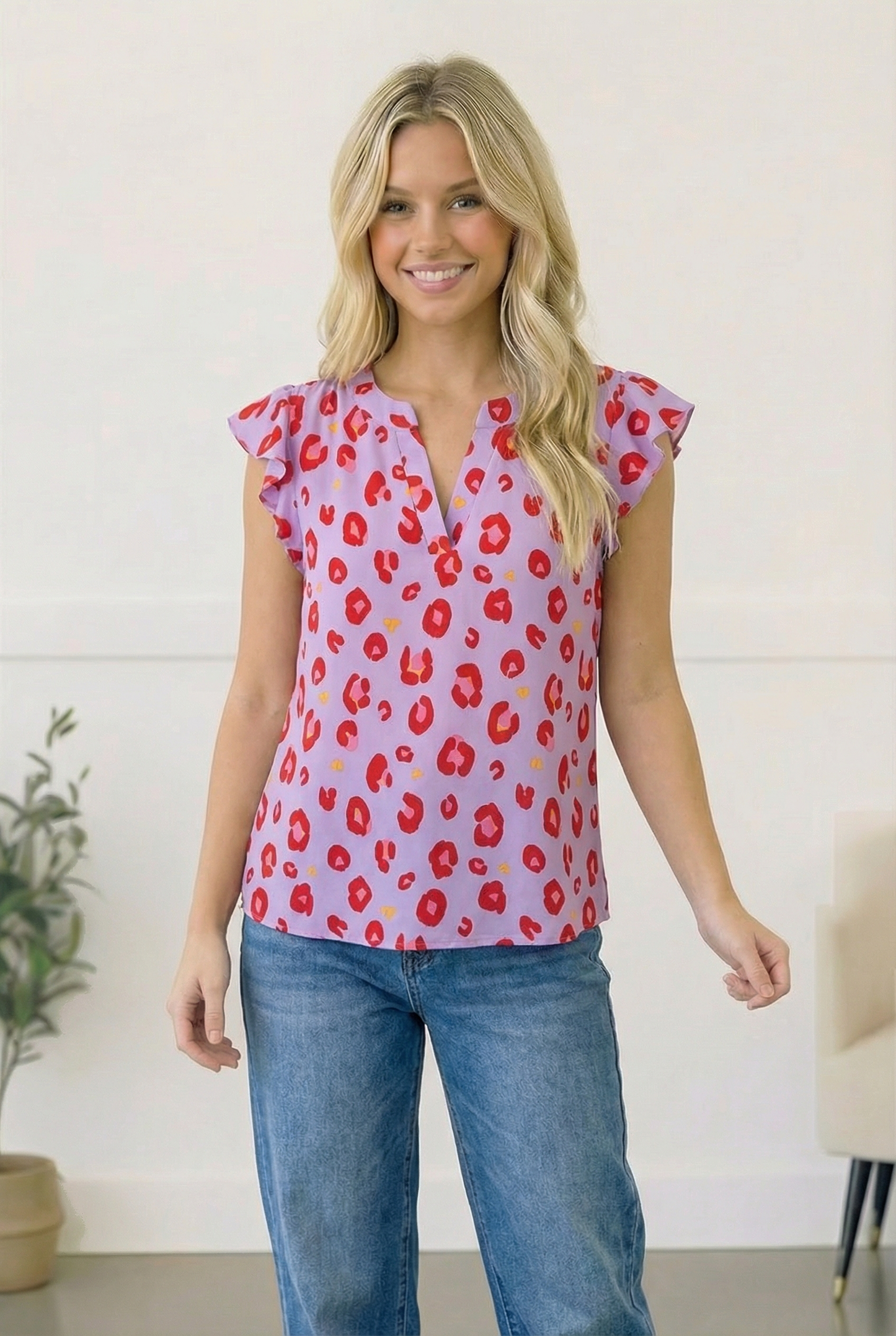 Woman wearing a pink blouse with red floral pattern and blue jeans indoors.