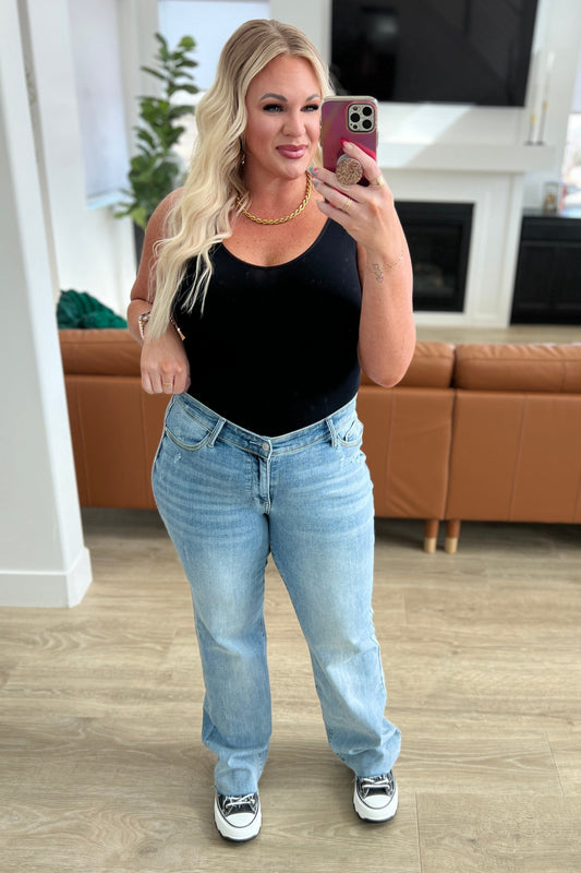 Women in black tank and High Rise V- Front straight Judy Blue jeans in a light wash color in a family room setting.